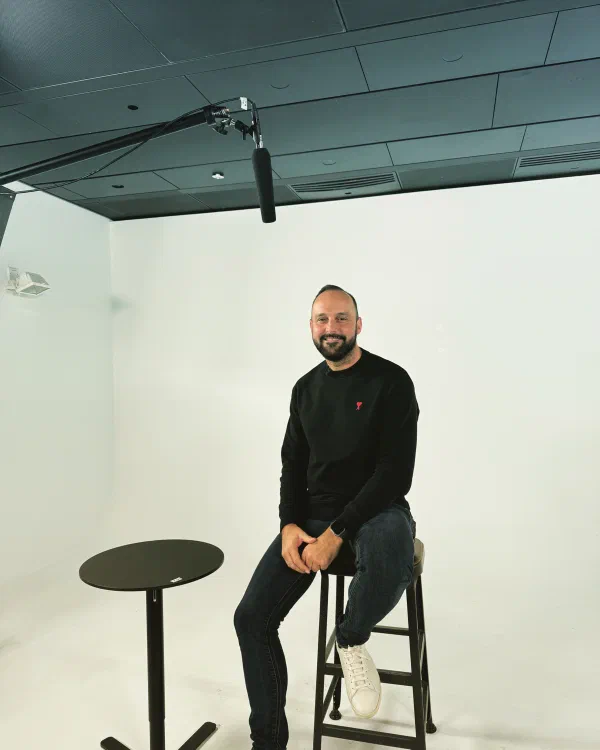 Mario Thomas seated on a stool under a boom microphone in a white studio