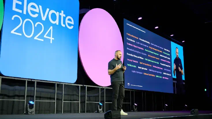 Mario Thomas on stage at Monday.com Elevate at ExCel London with a list of AI use cases on screen.