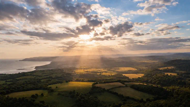 Aerial view of a landscape as clouds gradually clear, with sunlight revealing the underlying terrain, representing how a board-level diagnostic cuts through activity metrics to expose the organisation’s true AI position (Image generated by ChatGPT 5.2)