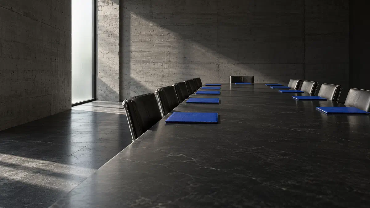A long black stone boardroom table in a concrete room with an electric-blue folder squared at every empty seat, for the briefing on what AI asks of each person who governs. (Image generated by ChatGPT 5)